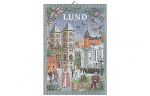 Produktbild: Handduk med motiv från Lund – domkyrkan, gamla hus, blommande grenar och en vattenkanna på tyget.