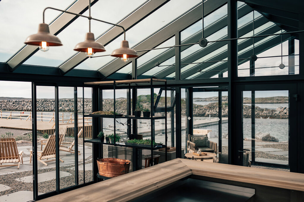 Interiör i svenskproducerat CL Alu isolerat uterum i hotellmiljö på ö i Norge, med glaspartier, svart aluminiumstomme och utsikt över hav och klippor.