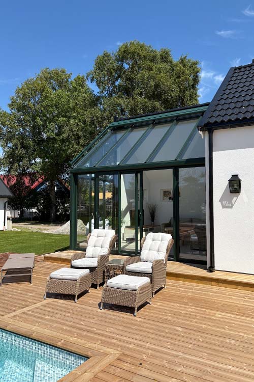 Uterum med stora glaspartier och pulpettak, med pool och solstolar placerade utanför – en perfekt plats för avkoppling och umgänge i trädgården.