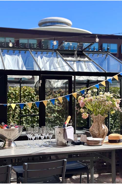 Inne på Hyllan, bland orangerierna på Malmö Arena Hotel, dukat för fest med bubbel, , dekorativa växter och Hyllies Vattentorn i bakgrunden.