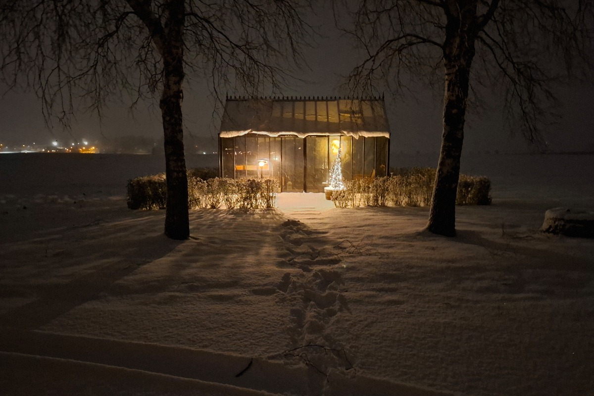 Antique-växthus från Classicum vintertid, belyst inifrån och omgivet av snö i öppet och väderutsatt landskap.