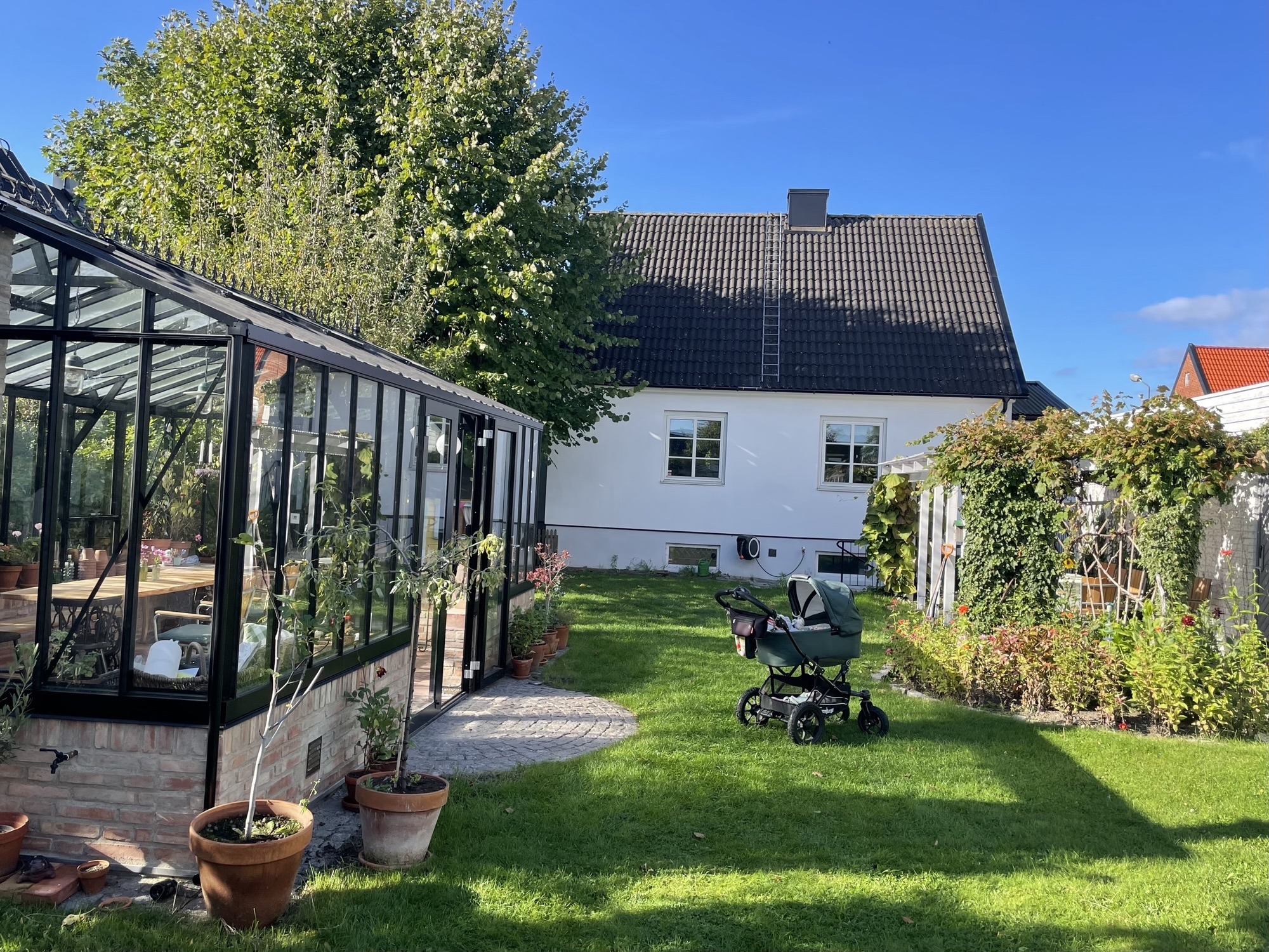 trädgård med växthus, vitt bostadshus och barnvagn på gräset